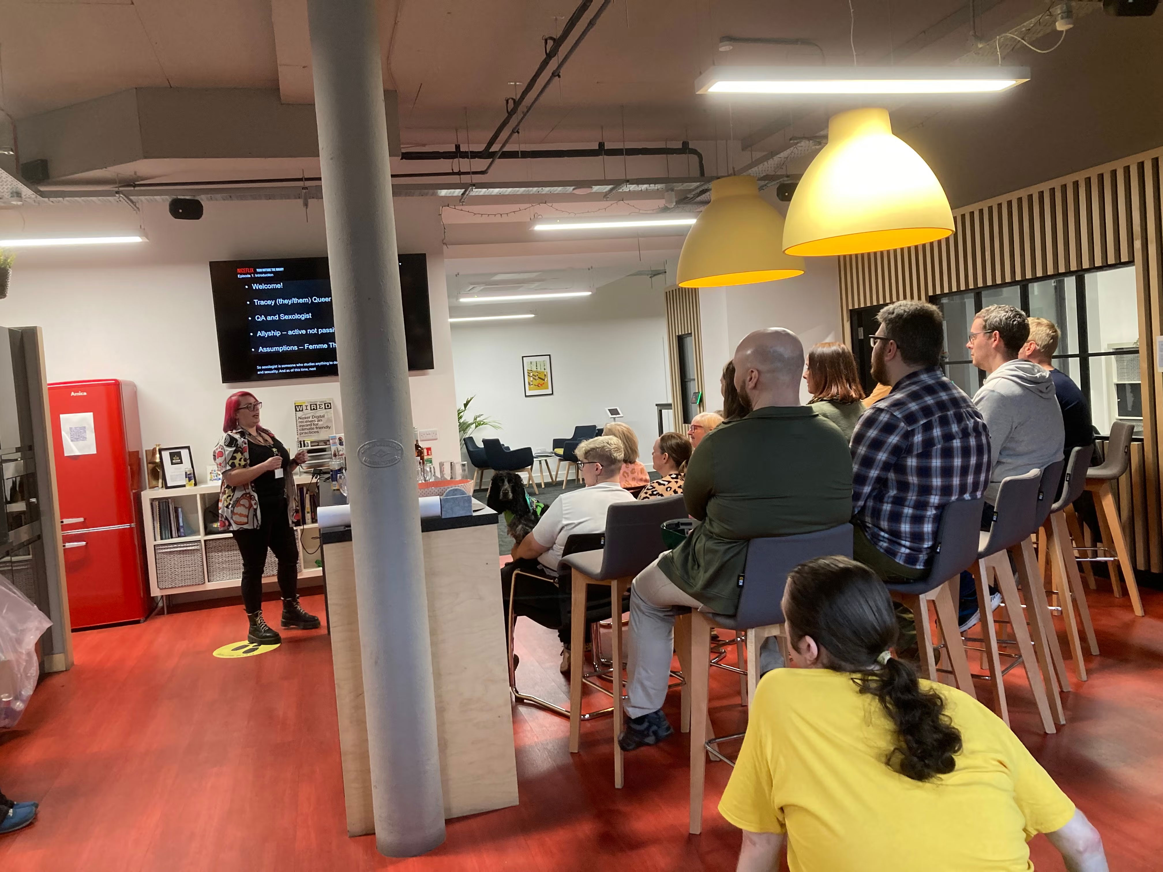 Tracey presenting to the audience. A vertical post stands mid-picture.