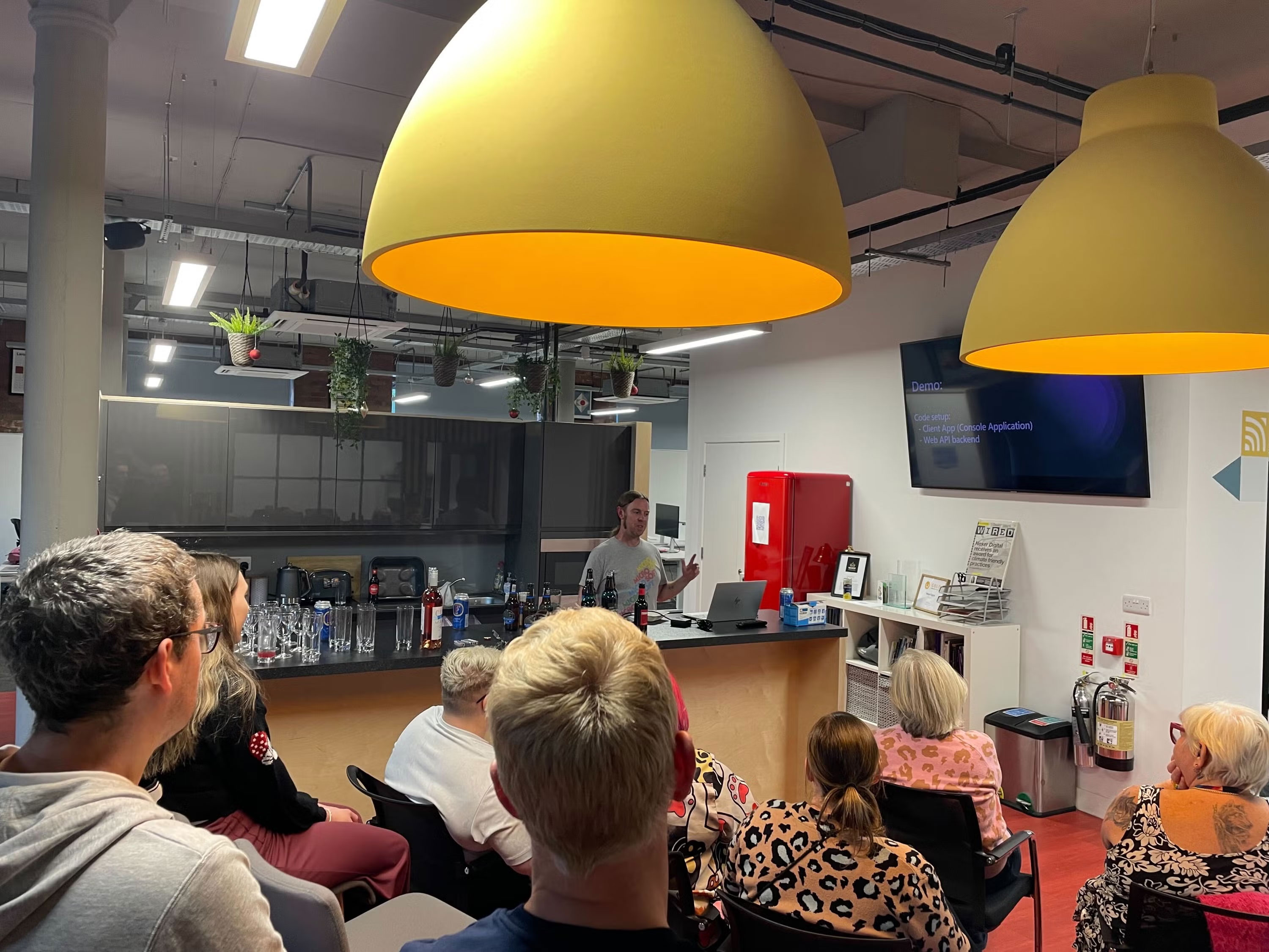 Audience watching Mike talk. Mike pointing to the screen, that reads 'Demo'