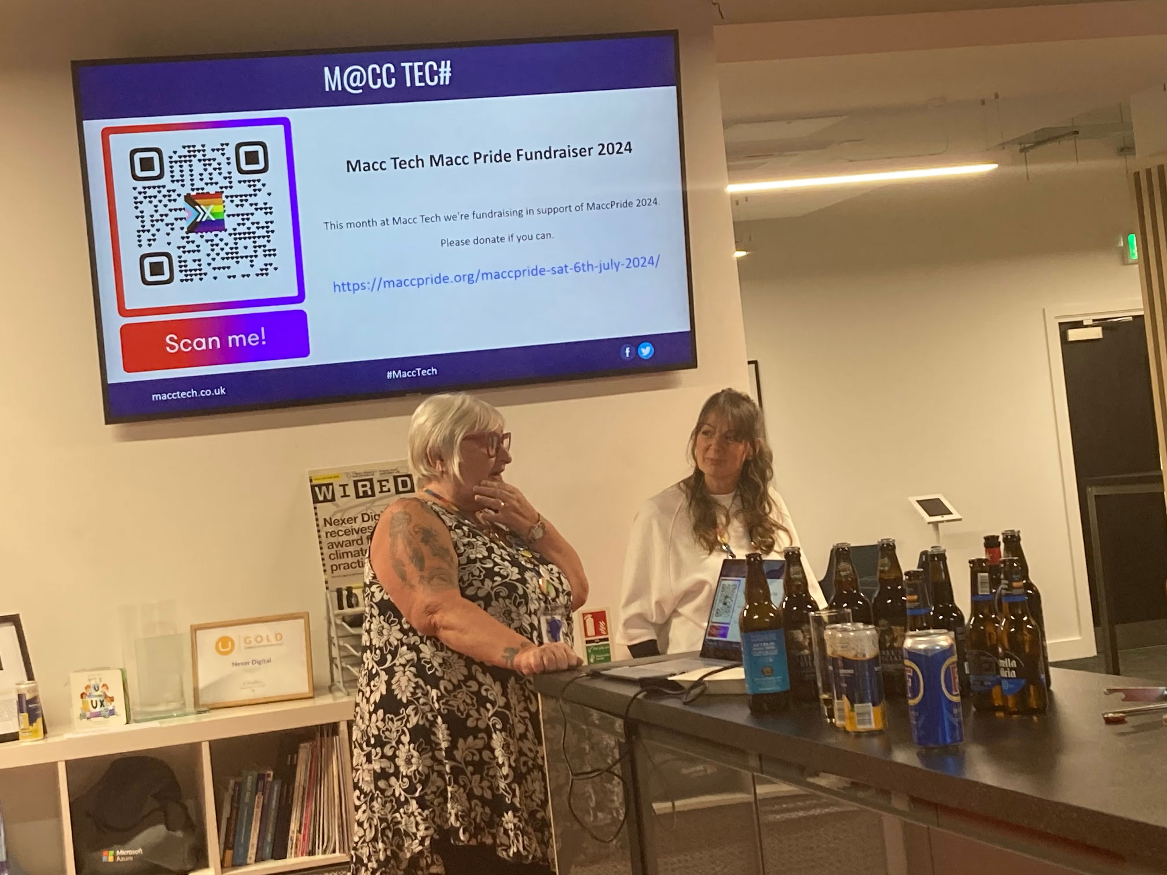 Sue and Jo from Macc Pride telling the audience about the organisation. Screen in background shows a donation QR code.