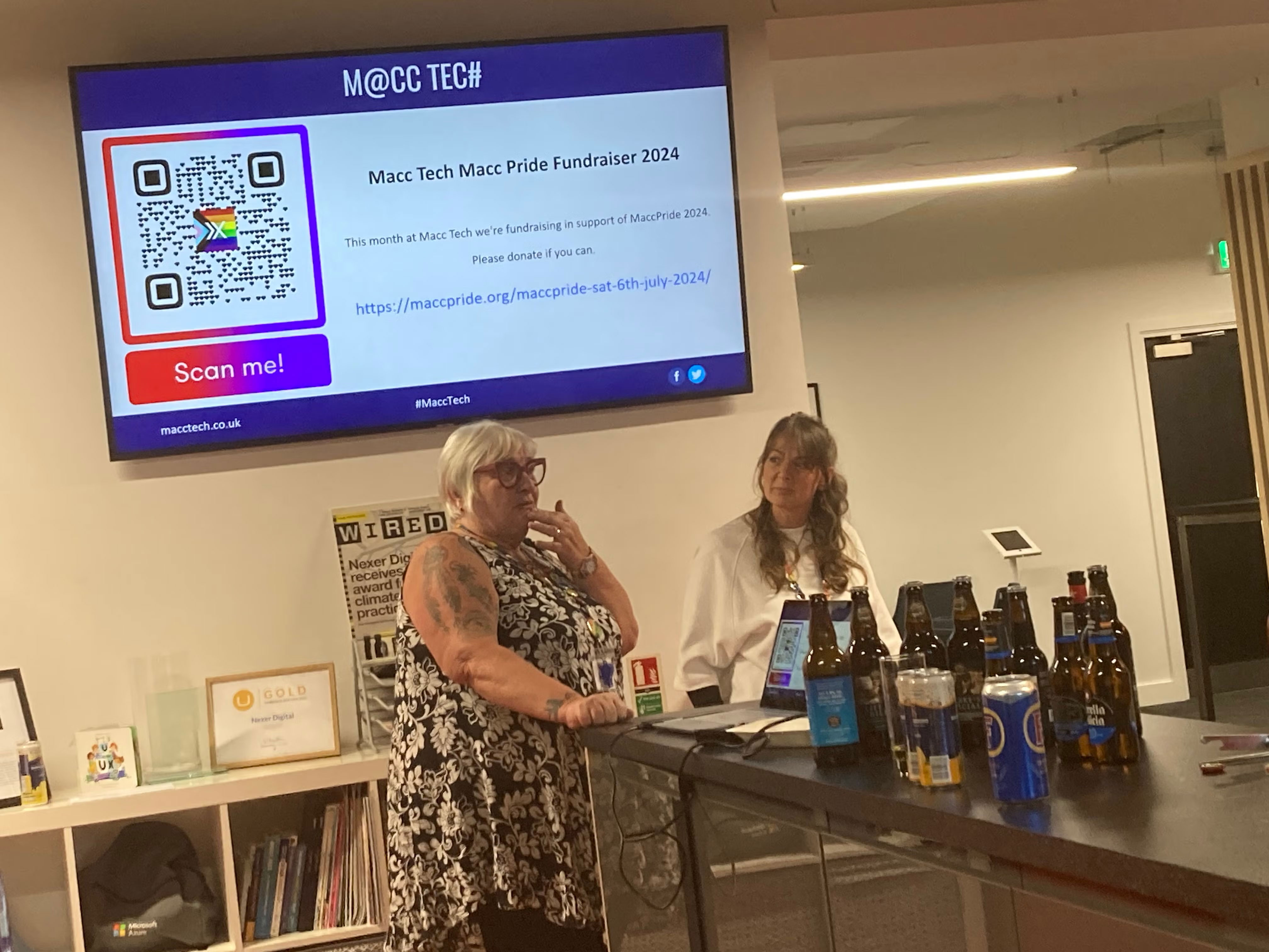 Sue and Jo from Macc Pride telling the audience about the organisation. Screen in background shows a donation QR code.