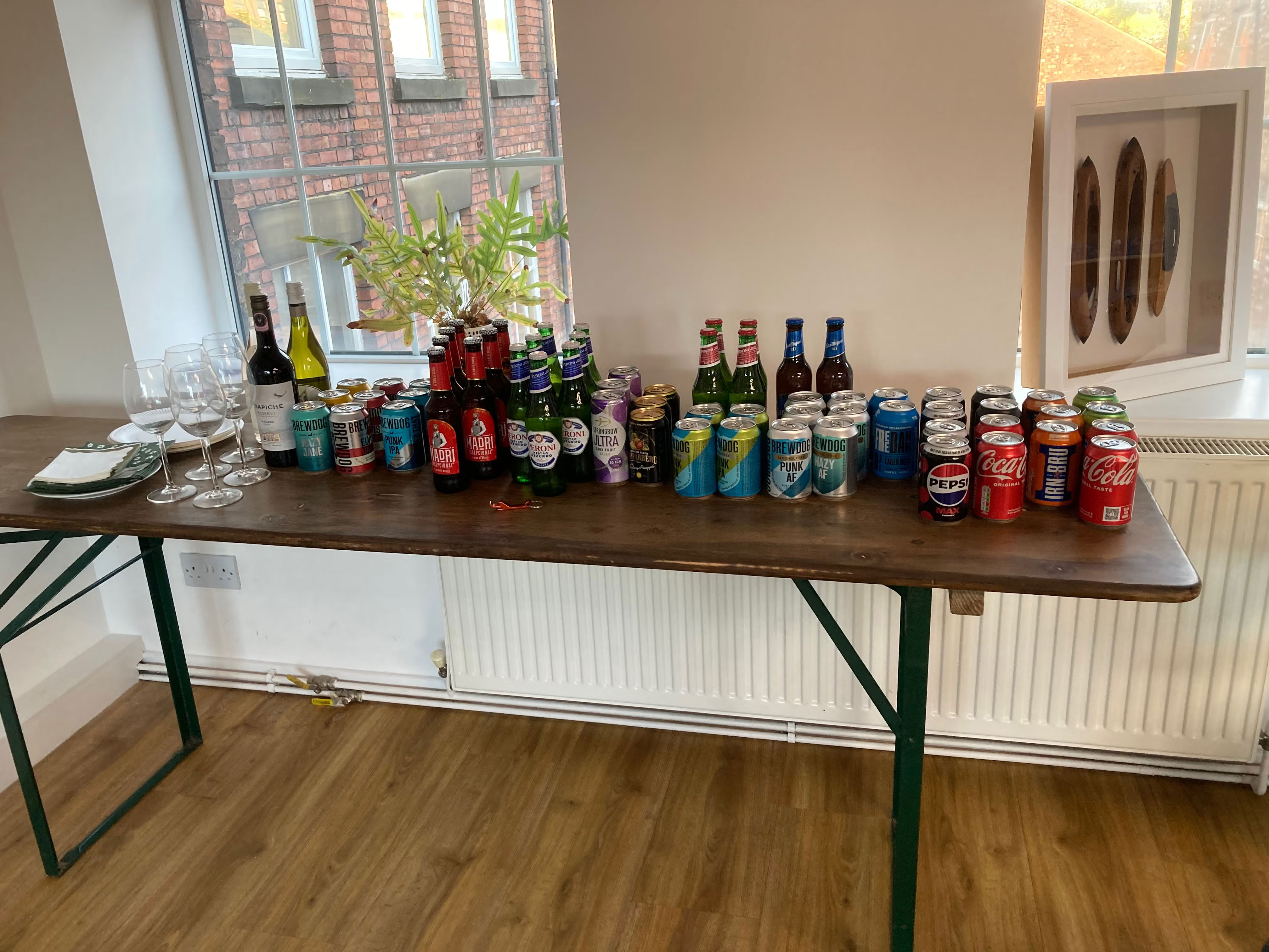 wine glasses, wine bottles, bottled and tinned beers, and soft drinks tins, on a table in front of a window. refreshments, courtesy of Blue Beck