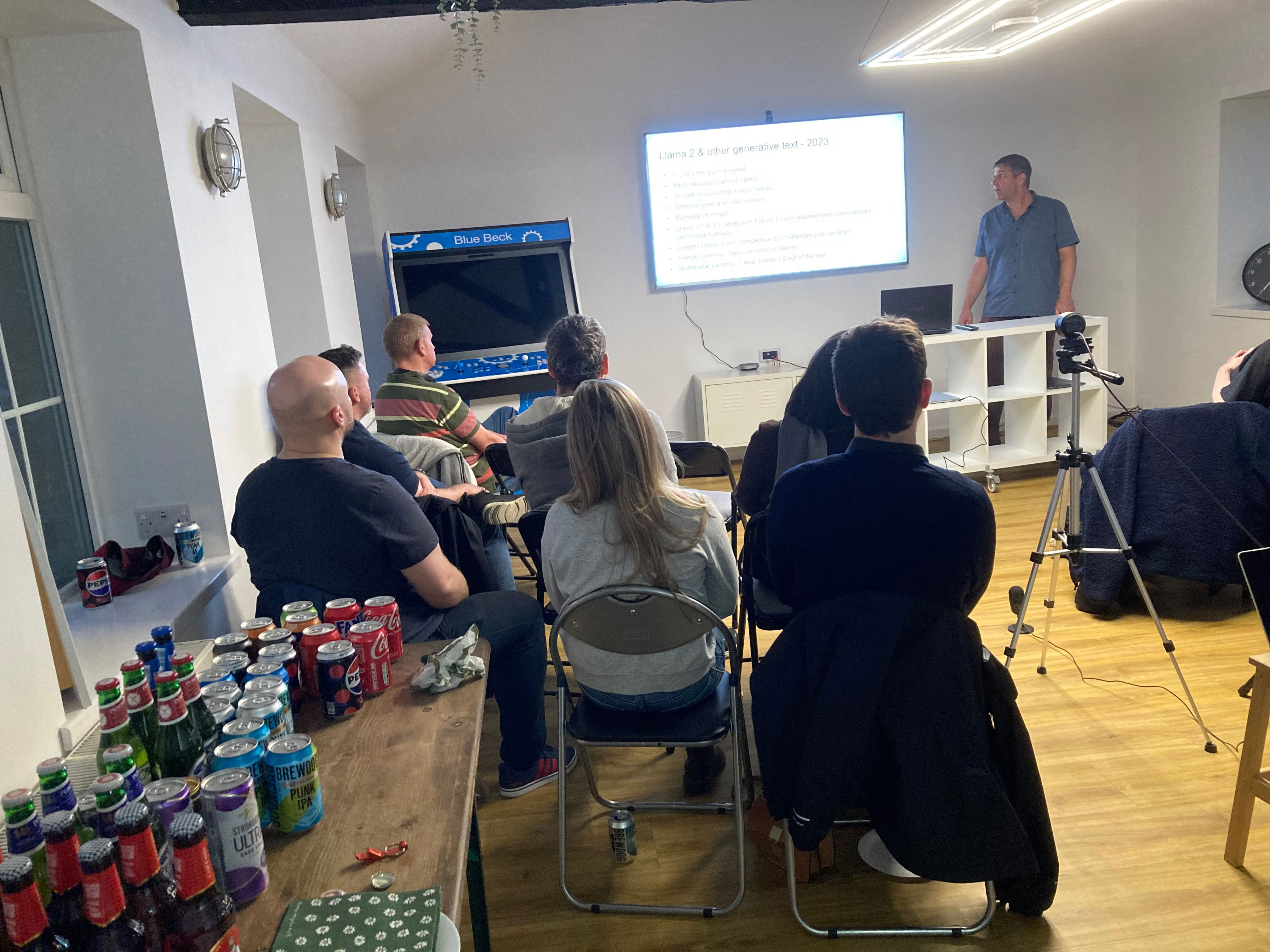 side view of drinks table, audience, screen, camera, Richard presenting