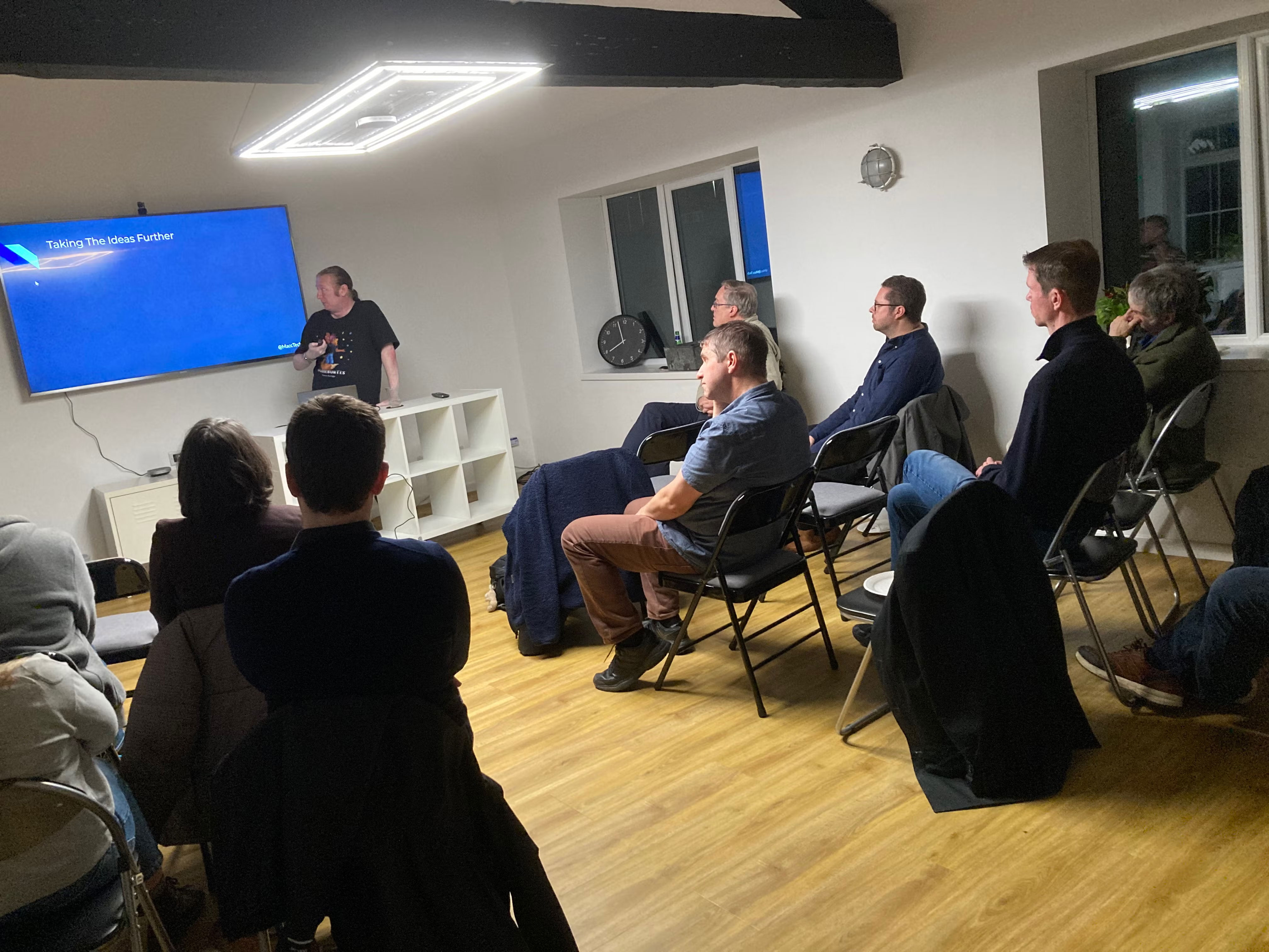 Terence glancing at his slide on screen. Audience watches.